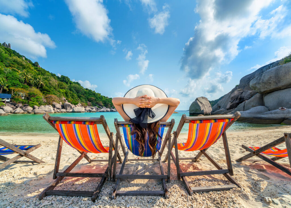 femme-vue-de-dos-allongee-sur-un-transat-avec-un-chapeau-devant-la-mer