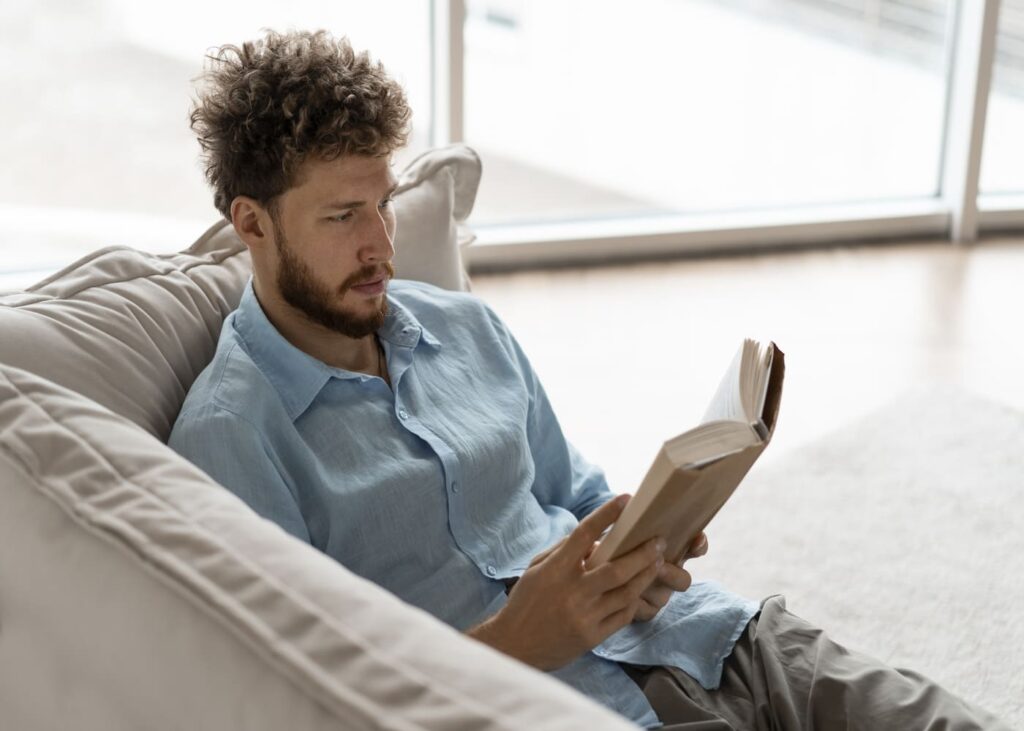 homme-allonge-dans-un-canape-qui-lit-un-livre