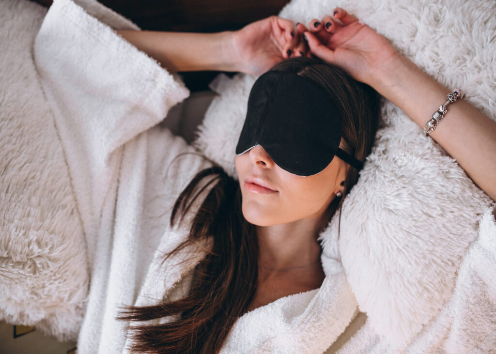 femme-allongee-dans-un-lit-avec-un-masque-de-nuit