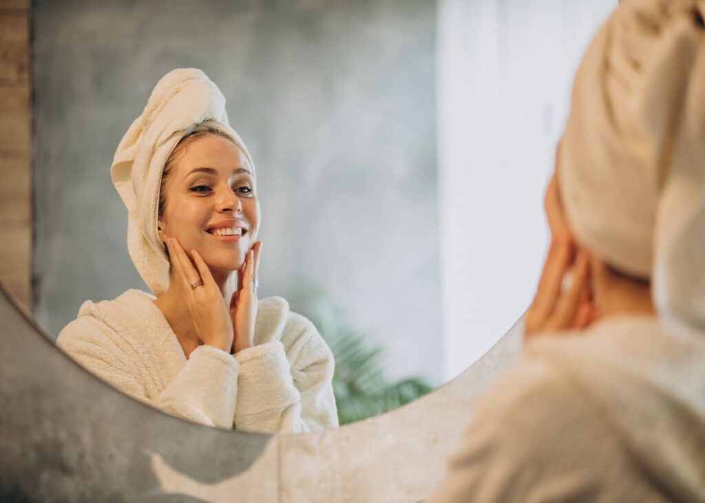 femme-en-peignoir-avec-une-serviette-sur-la-tete-qui-sourit-en-se-regardant-dans-le-miroir