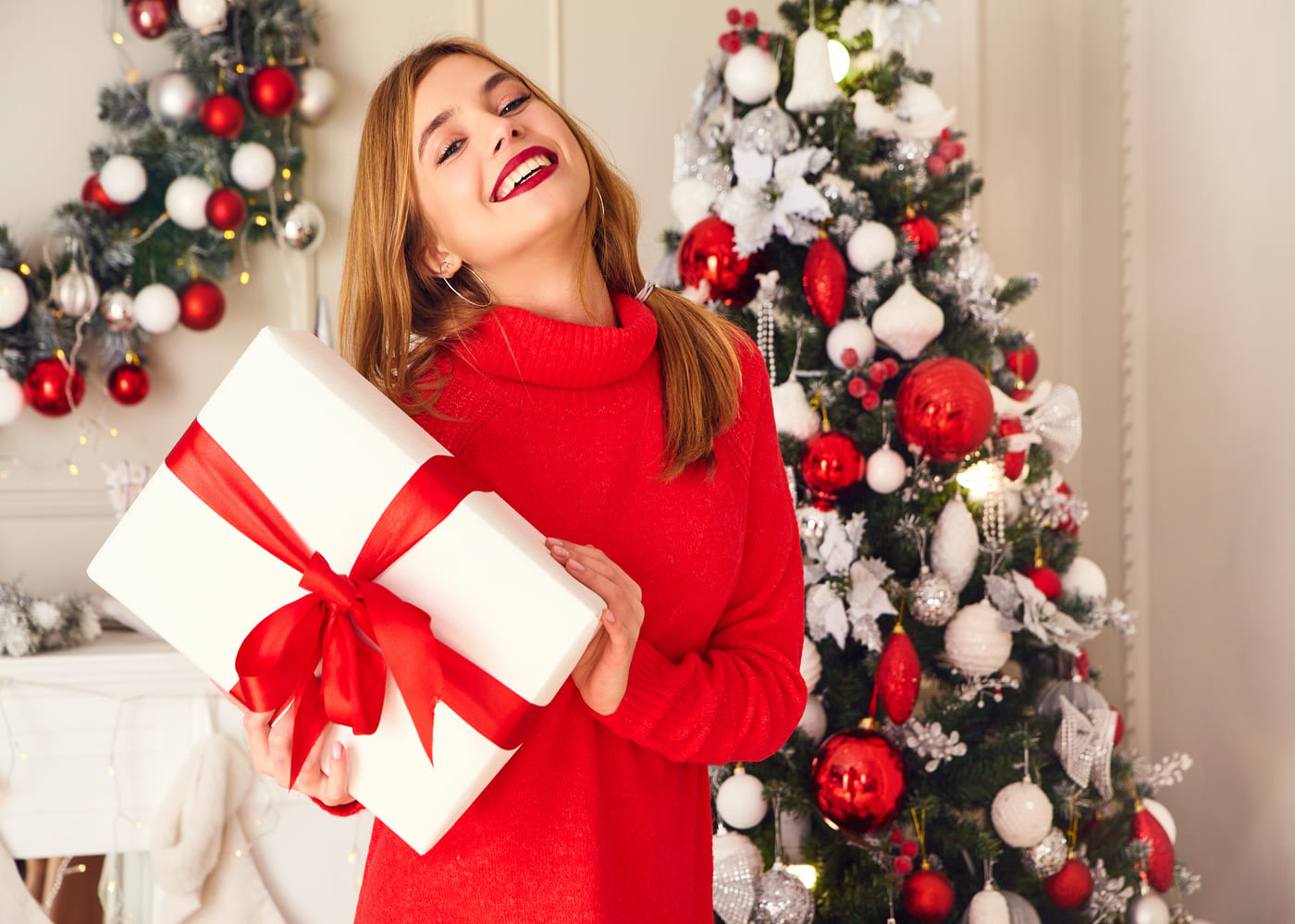 femme-en-pull-rouge-heureuse-en-train-de-tenir-un-cadeau-devant-un-sapin-de-noel