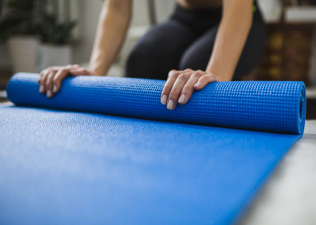 femme-qui-enroule-un-tapis-de-gym-bleu-au-sol