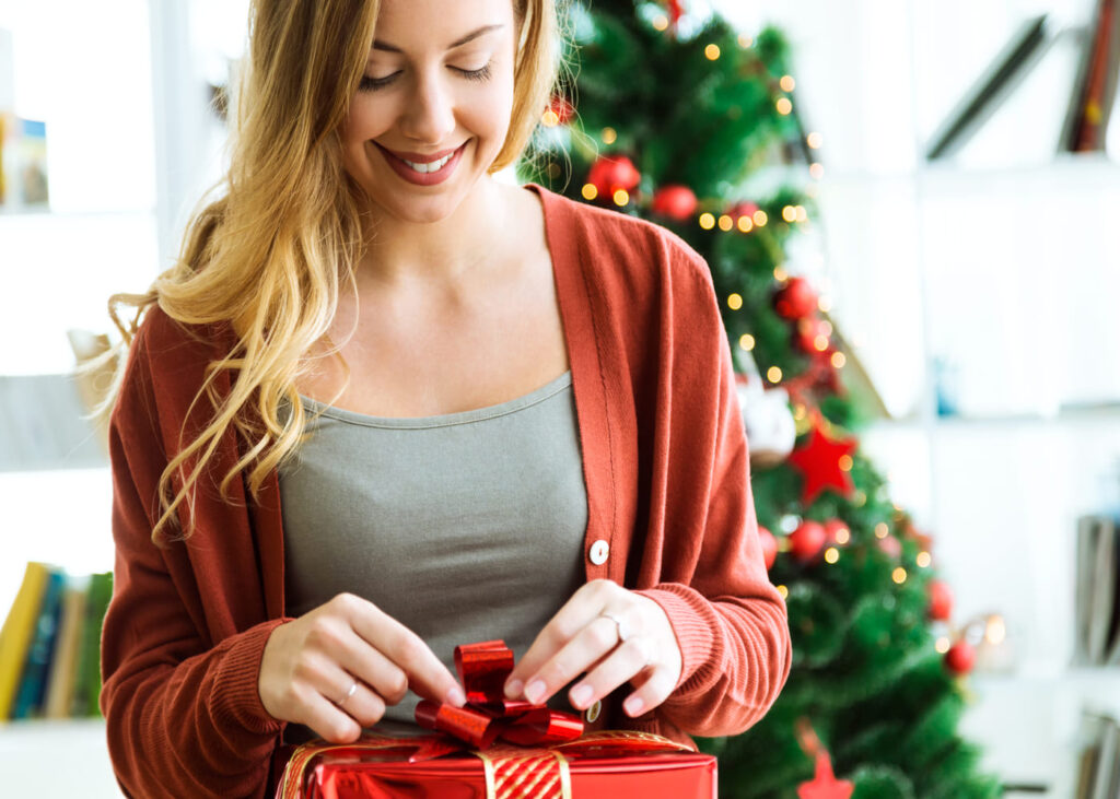 femme-qui-ouvre-un-cadeau-rouge-devant-un-sapin-de-noel