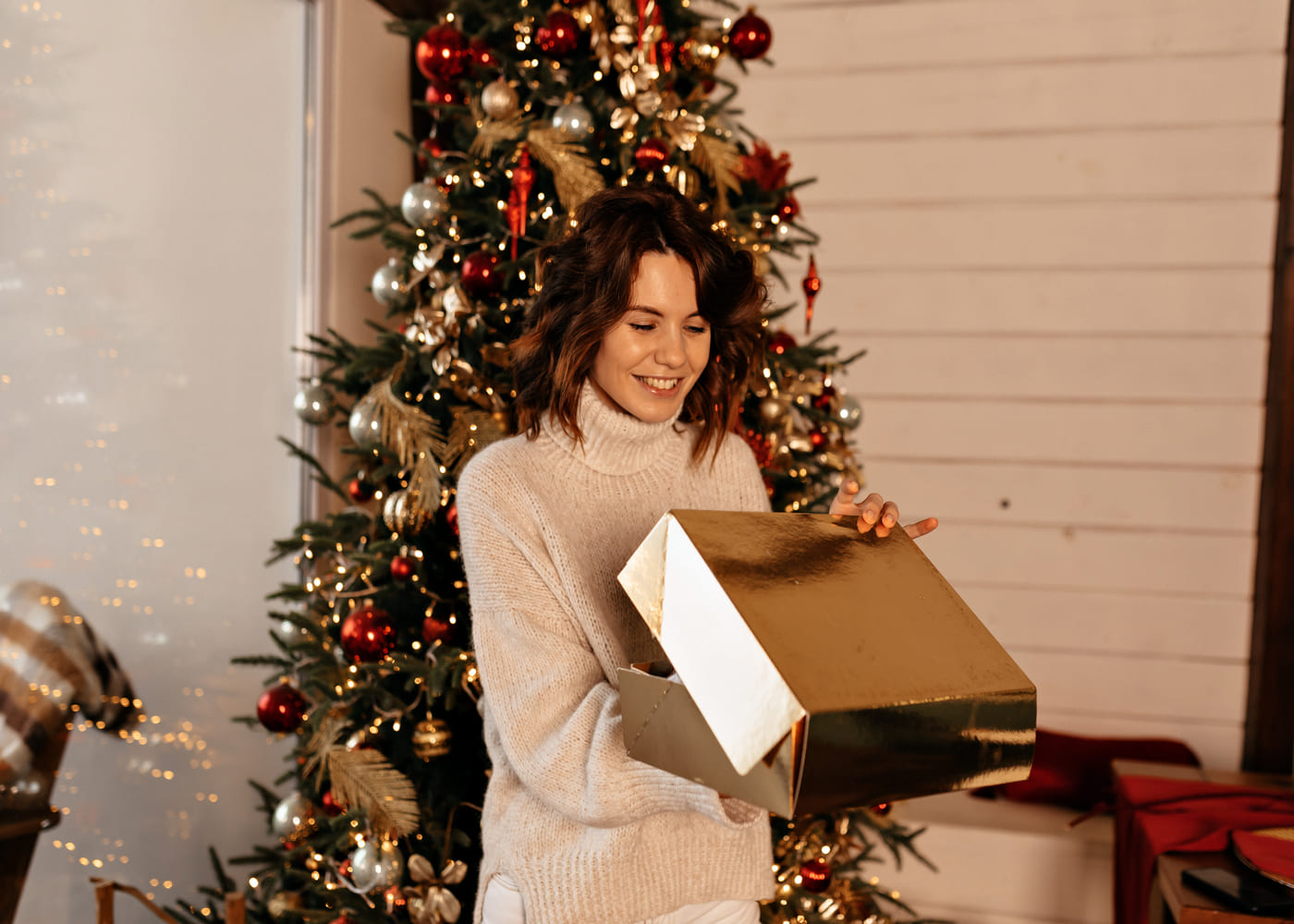 femme-qui-sourit-en-deballant-son-cadeau-de-noel-devant-le-sapin