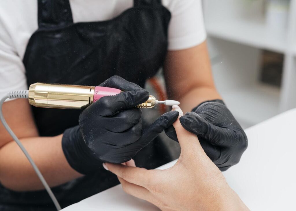 femme-qui-utilise-une-ponceuse-sur-l-ongle-du-pouce-de-sa-cliente.jpg