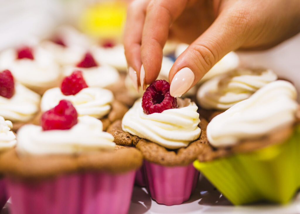 gros-plan-d-une-main-de-femme-qui-met-une-framboise-sur-un-cupcake