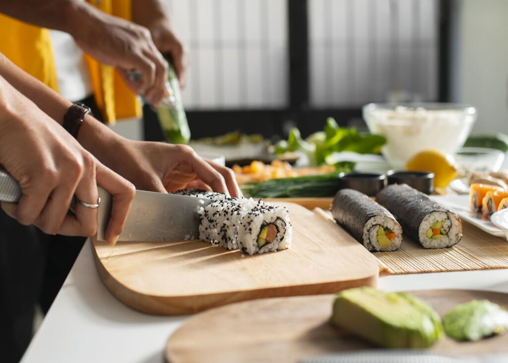 gros-plan-de-deux-mains-en-train-de-couper-des-sushis-sur-une-table-remplis-d-ingredients