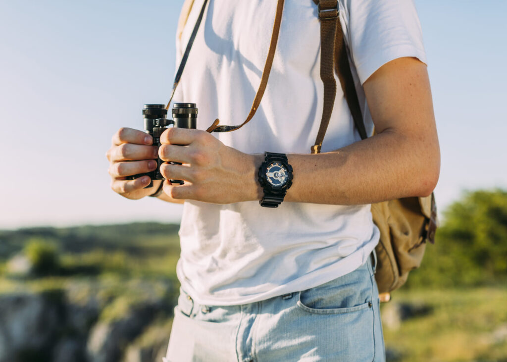 gros-plan-homme-qui-tient-des-jumelles-avec-une-montre-sur-son-poignet-en-pleine-nature.jpg