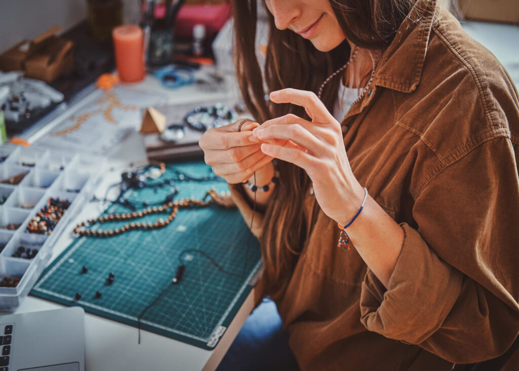 gros-plan-sur-une-femme-souriante-qui-cree-un-bijou-avec-des-perles