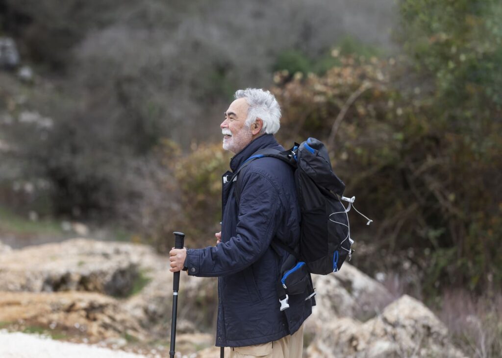 homme-age-en-train-de-faire-une-randonnée-avec-en-tentant-des-batons-de-marche-et-portant-un-sac-a-dos