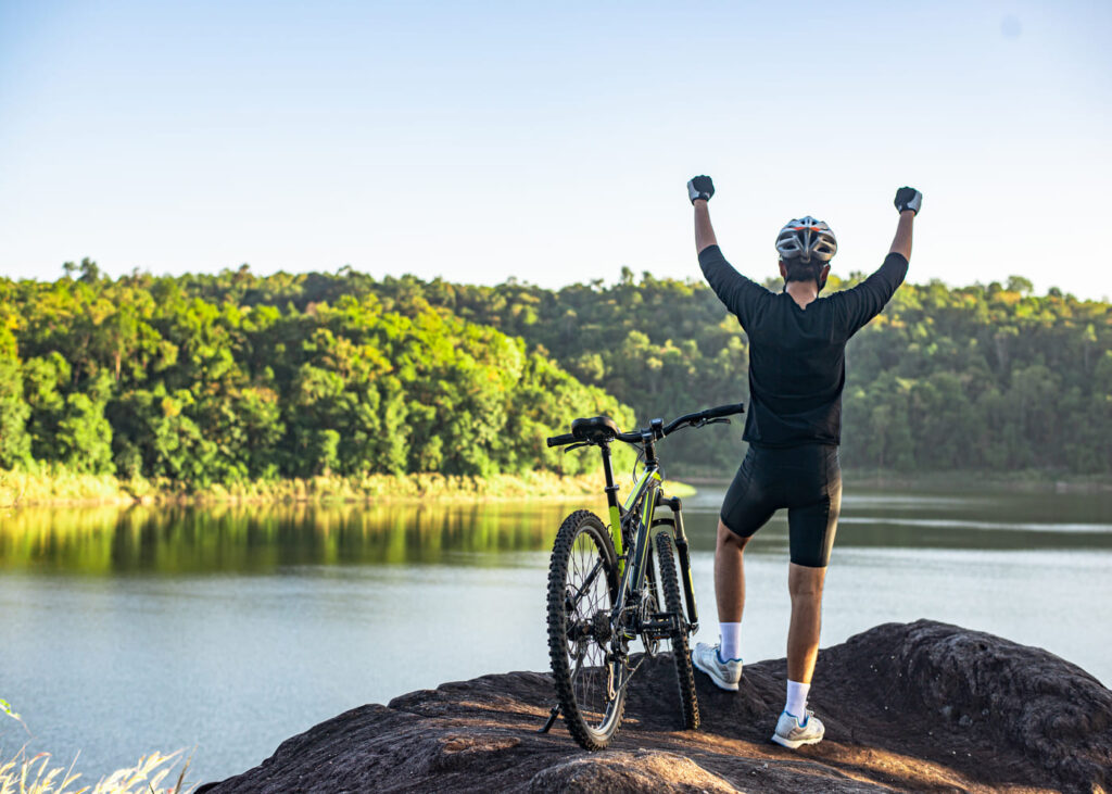 homme-avec-son-velo-qui-leve-les-bras-devant-un-lac