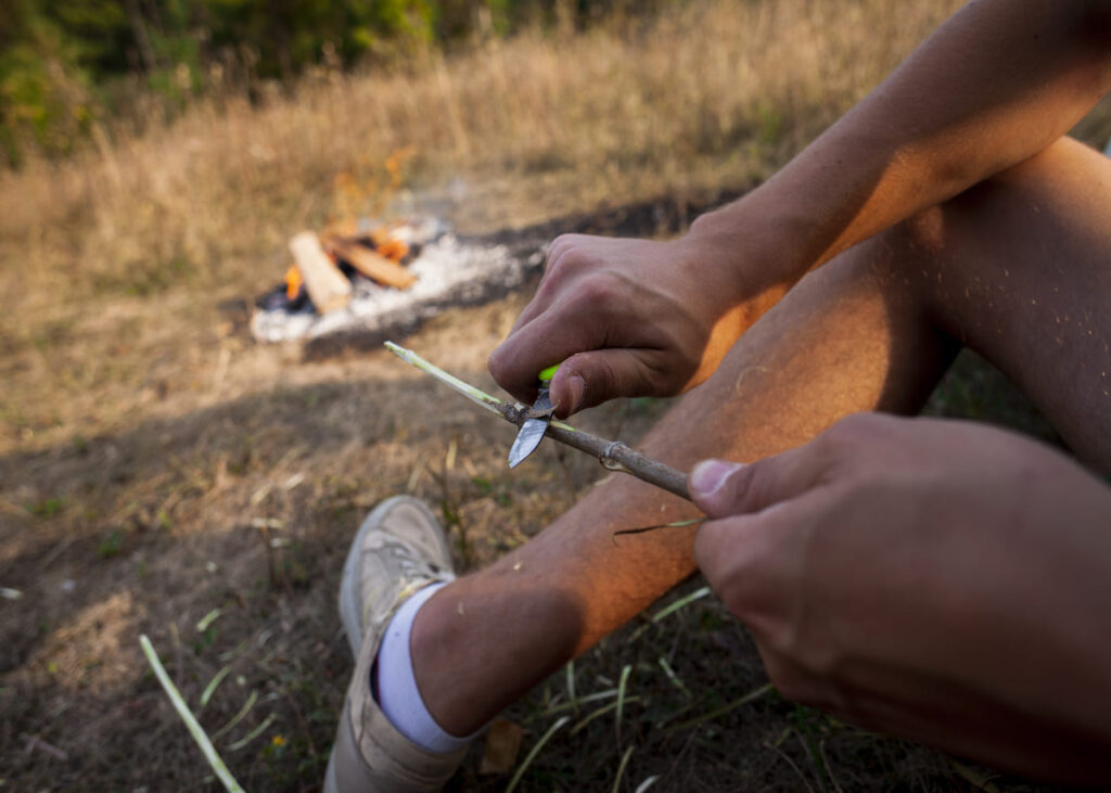 homme-en-bivouac-qui-sculpte-un-baton-en-bois.jpg