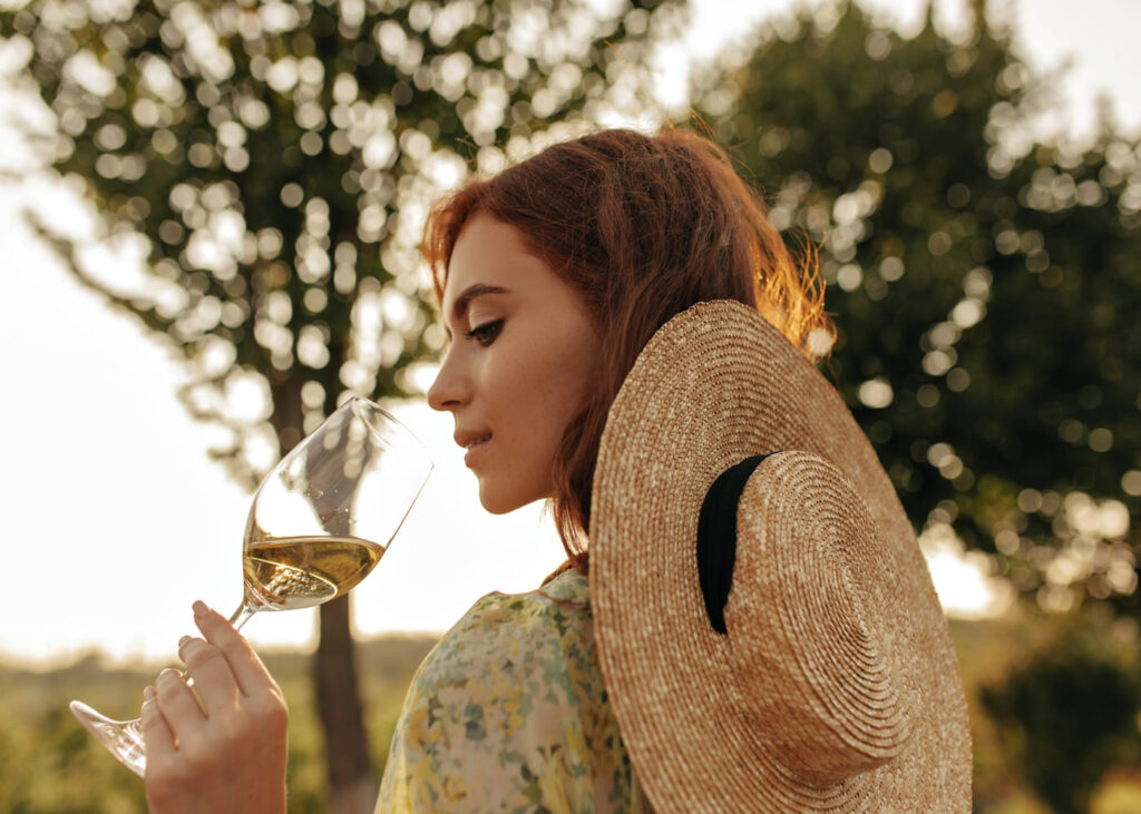 jeune-femme-avec-un-chapeau-de-paille-qui-boit-un-verre-de-vin-en-pleine-nature