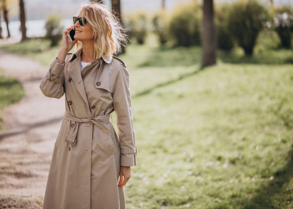 femme-blo,de-portant-un-trench-et-des-lunettes-de-soleil-qui-telephone-dans-un-parc