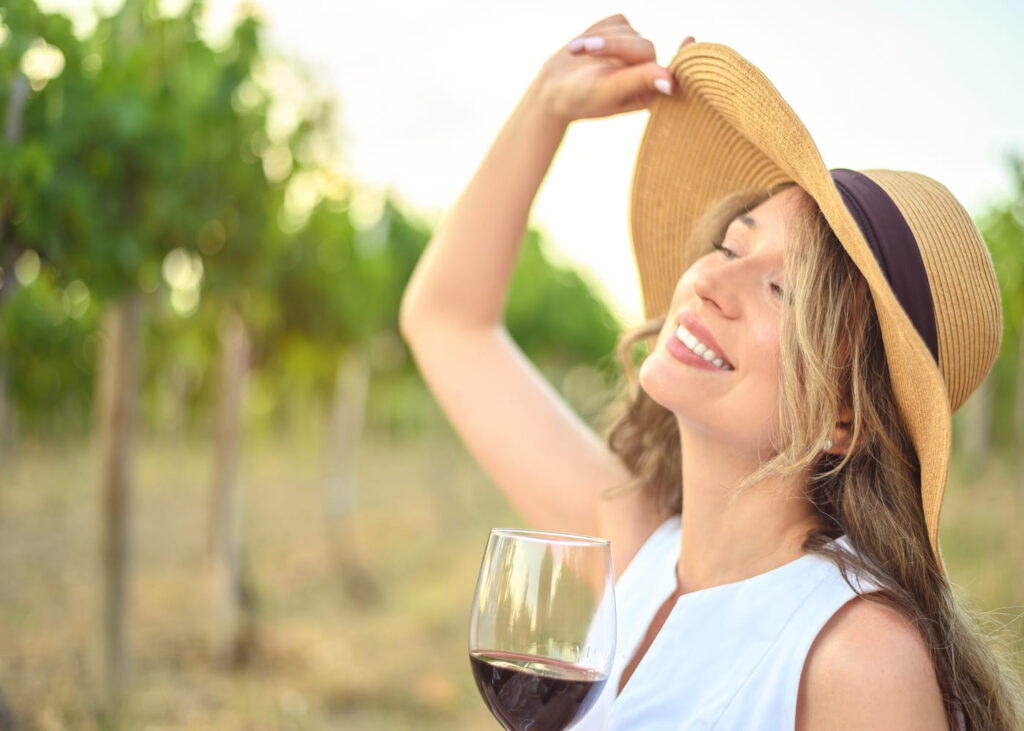 femme-blonde-avec-un-chateau-de-paille-qui-tient-un-verre-de-vin-dans-un-vignoble