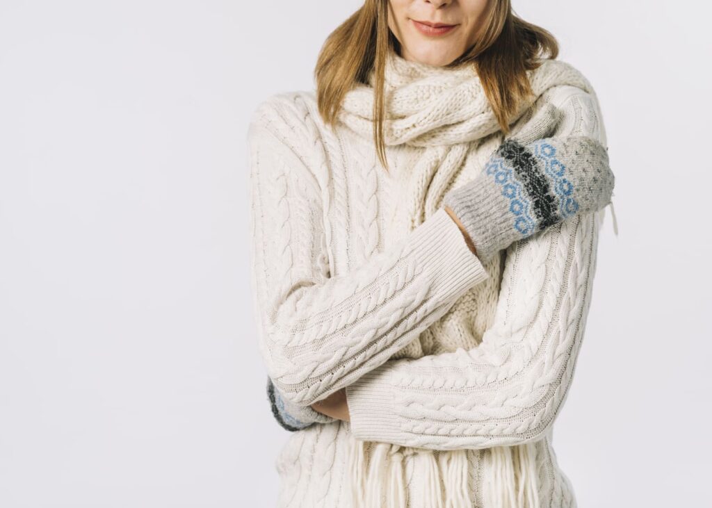 femme-en-pull-blanc-et-gants-qui-se-tient-pour-se-rechauffer