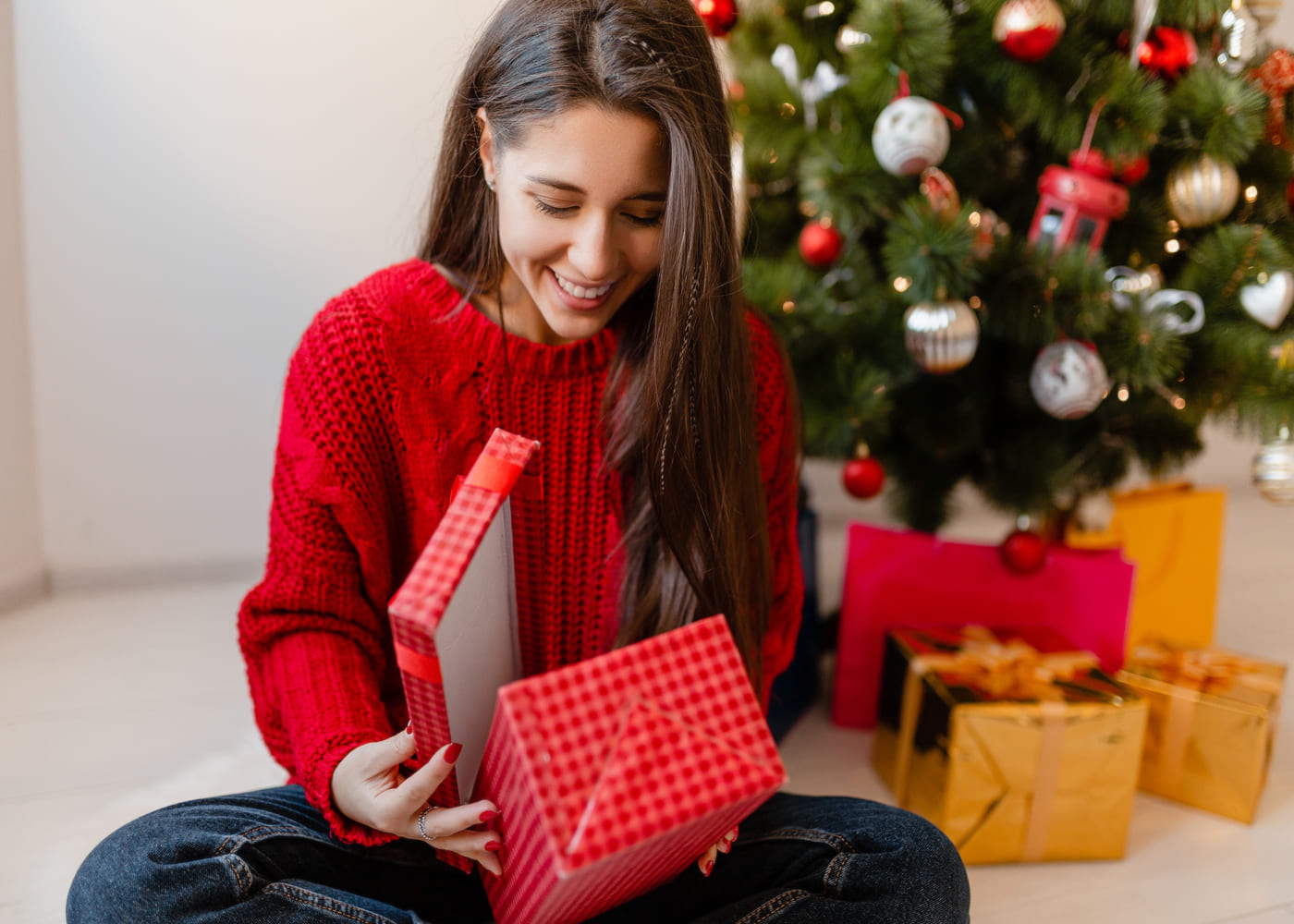 femme-en-pull-rouge-qui-ouvre-son-cadeau-de-noel-devant-le-sapin
