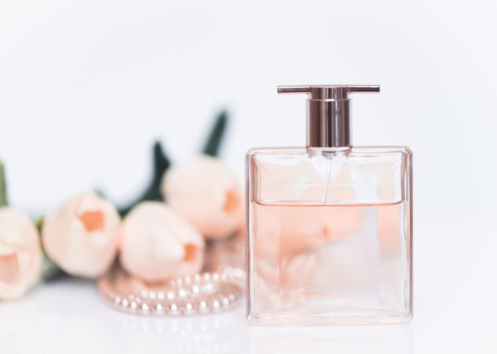 gros-plan-d-un-parfum-rose-avec-des-roses-et-un-collier-de-perles-en-arriere-plan