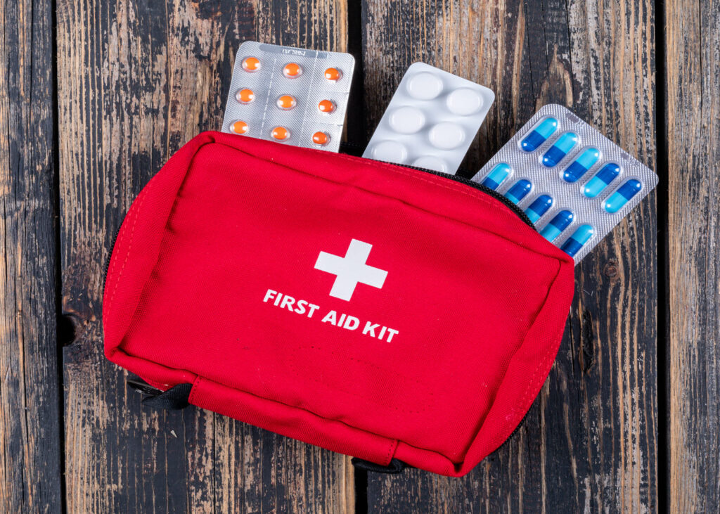 trousse-de-premier-secours-rouge-aec-des-plaquettes-de-medicaments-qui-depasse-posee-sur-une-table-en-bois