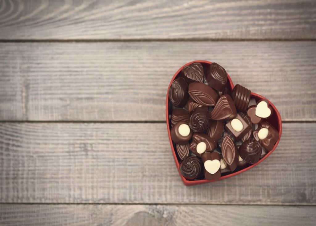 boite-en-coeur-rouge-remplie-de-chocolats-sur-un-fond-en-bois-gris
